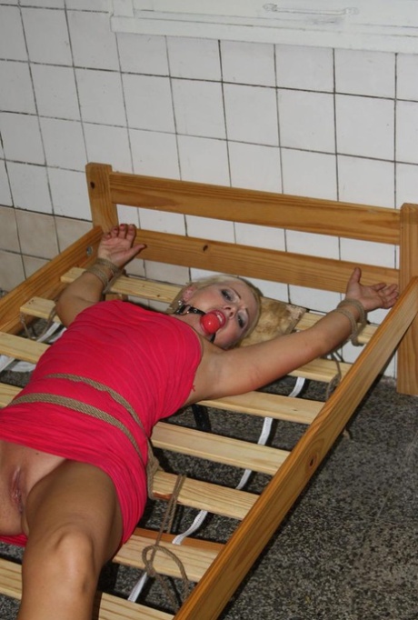 Ball gagged blond female struggles against rope restraints with dress hiked up 66543214